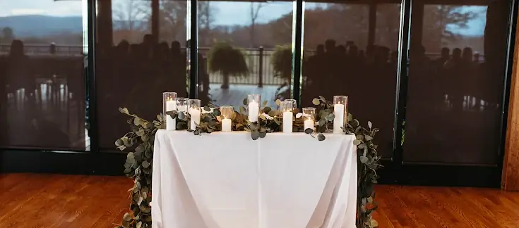 Sweetheart table with eucalyptus garland and pillar candles by the windows